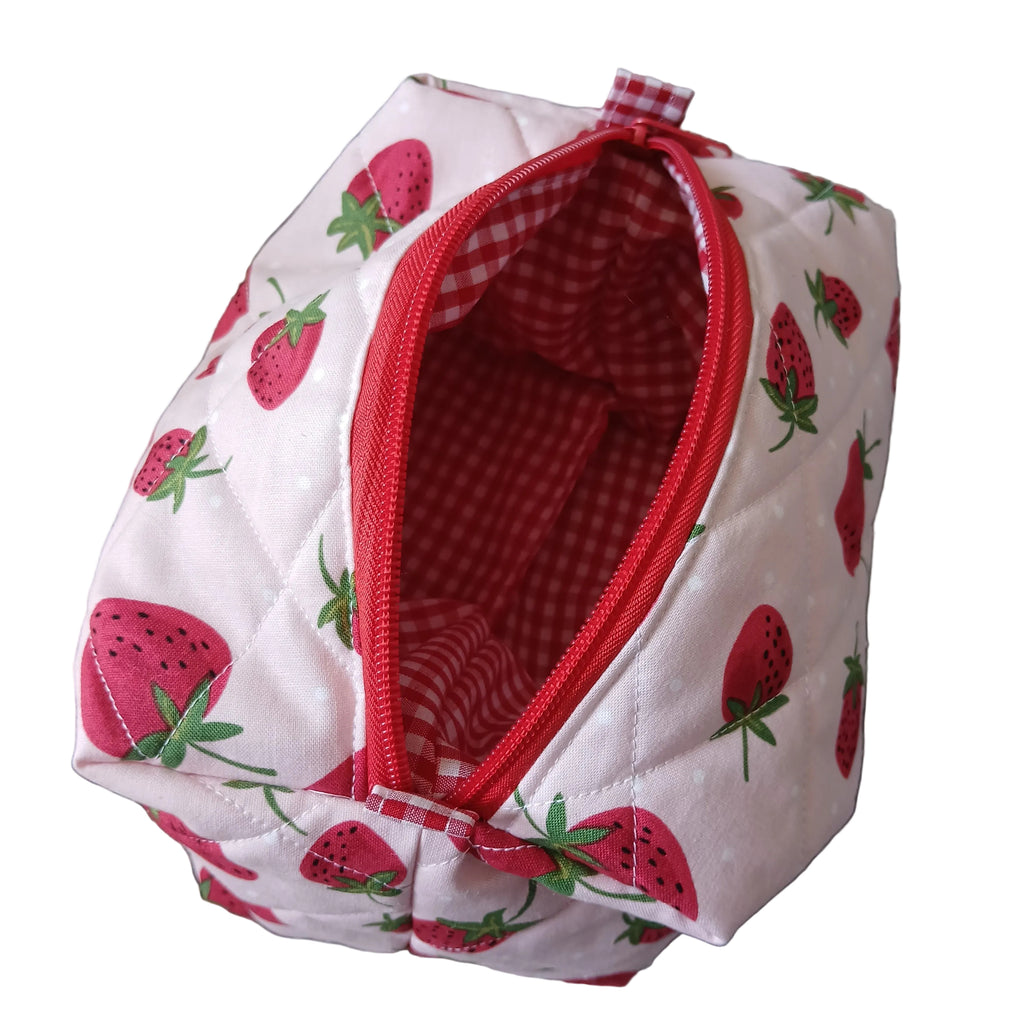 Small pouch with strawberry pattern and red zipper on a textured surface