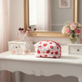 Makeup bag with strawberry pattern on a vanity table with mirror and flowers.